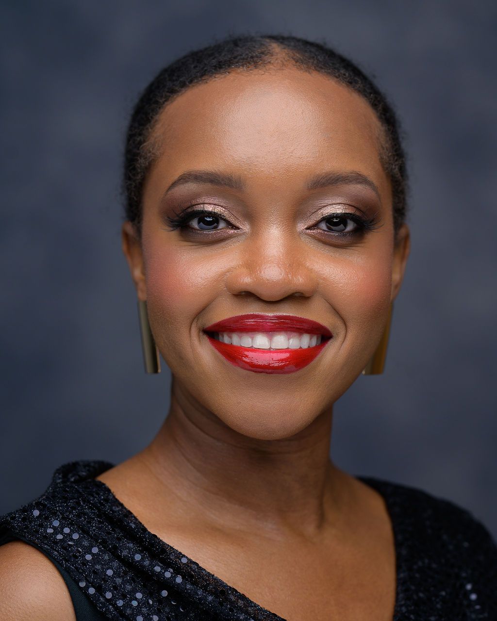 Woman with swept-back hair, luminous skin, softly defined eyes, and bright red lipstick.