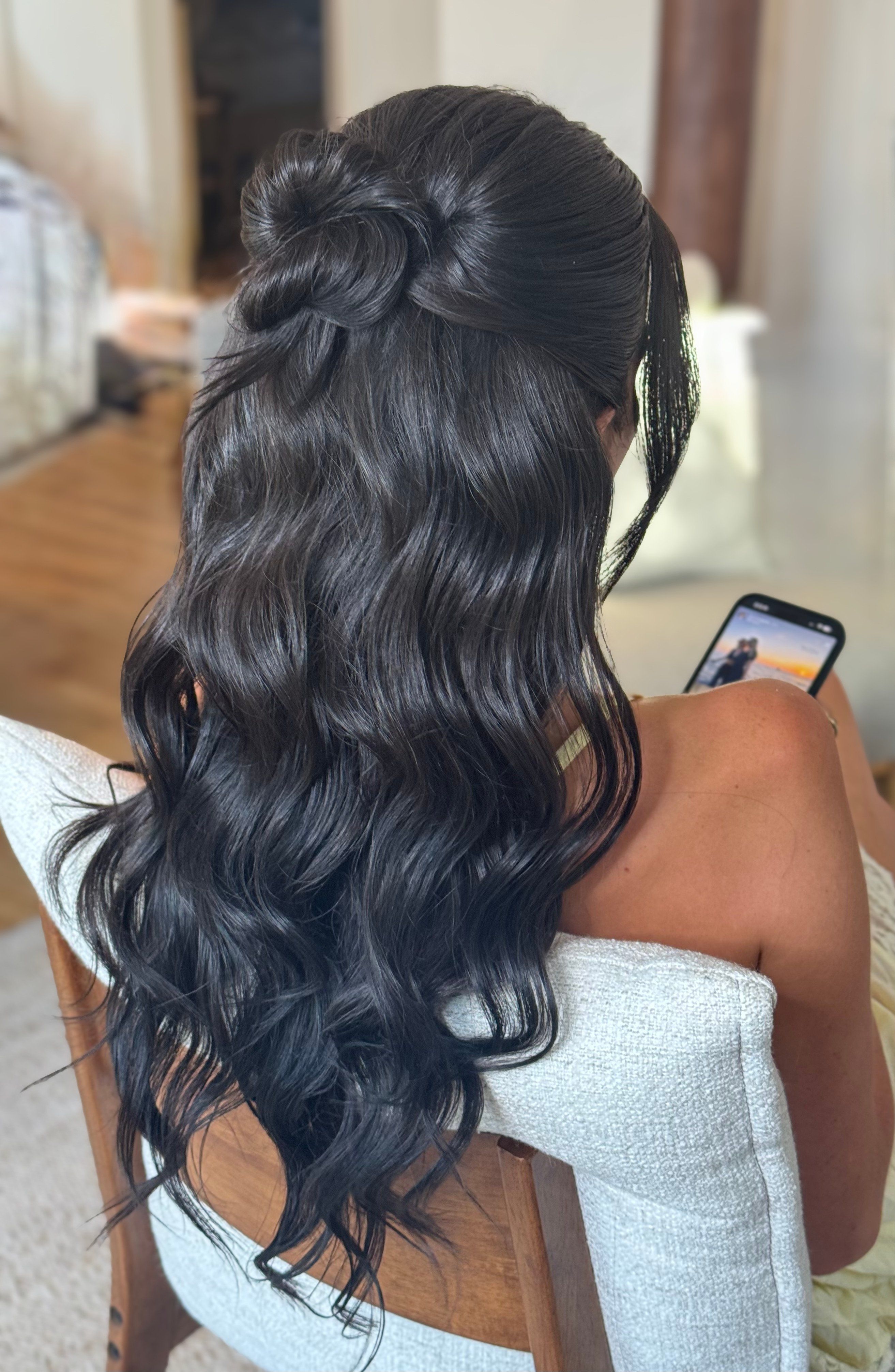 Back view of long black hair styled in glossy waves with a half-up twist.