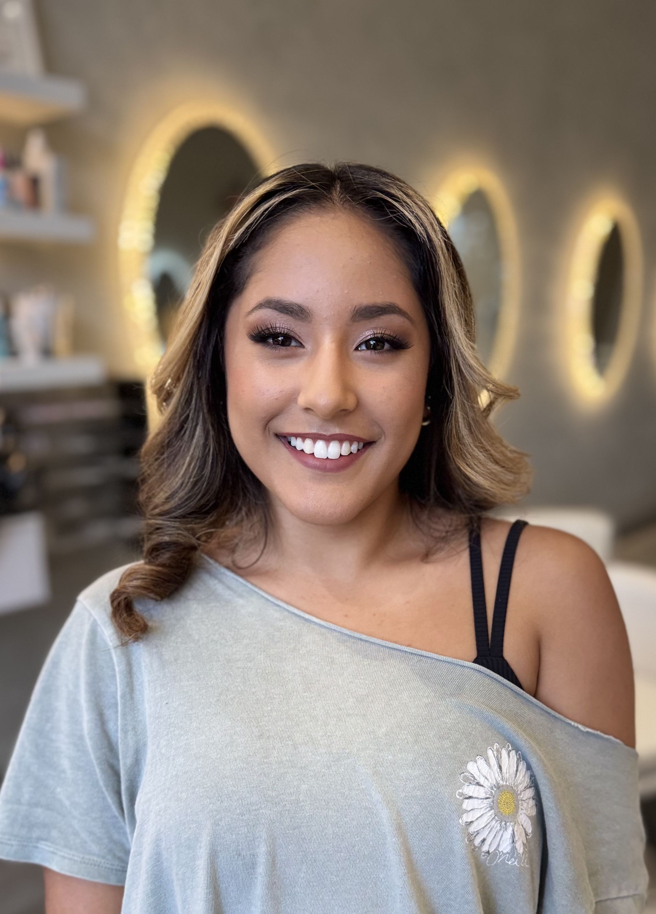 Smiling woman with straight dark hair and luminous neutral makeup in a salon.