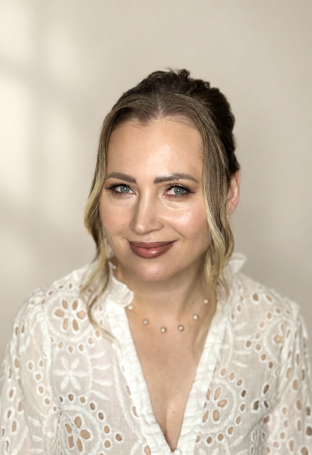 Woman with a swept updo and soft rose-toned makeup wearing a white lace robe.