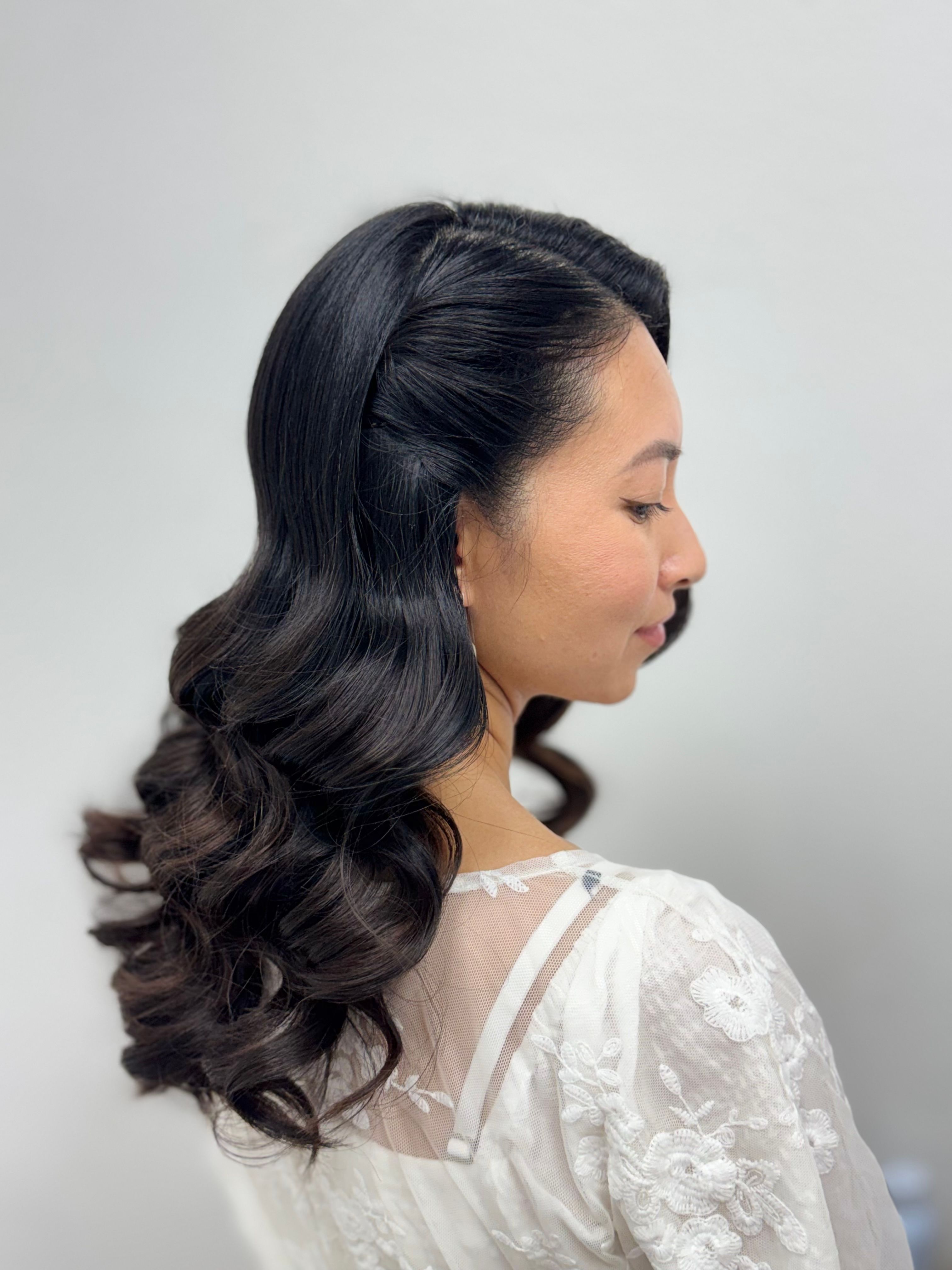 Side-back view of long dark curls styled with a twisted half-up detail.