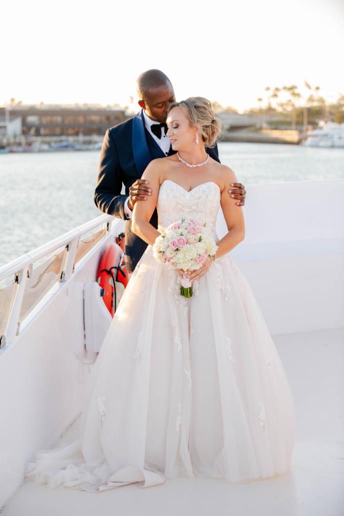 Bride with a curled updo, veil, and soft makeup standing with the groom by the water.