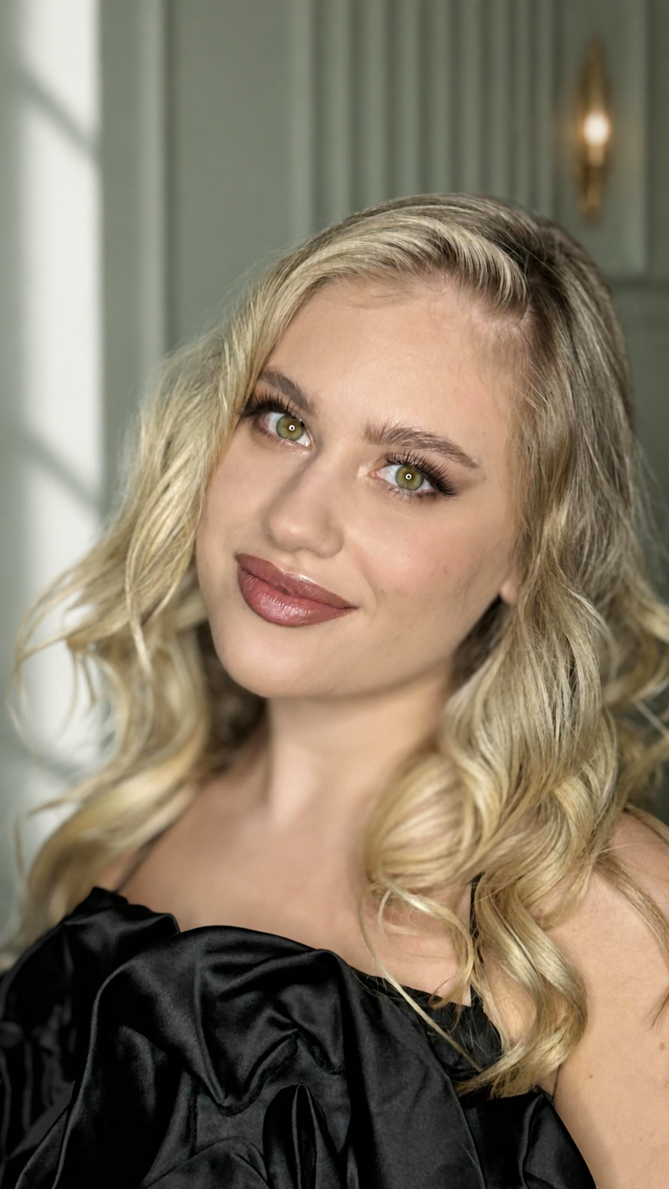 Blonde woman wearing long side-swept waves with soft neutral makeup.