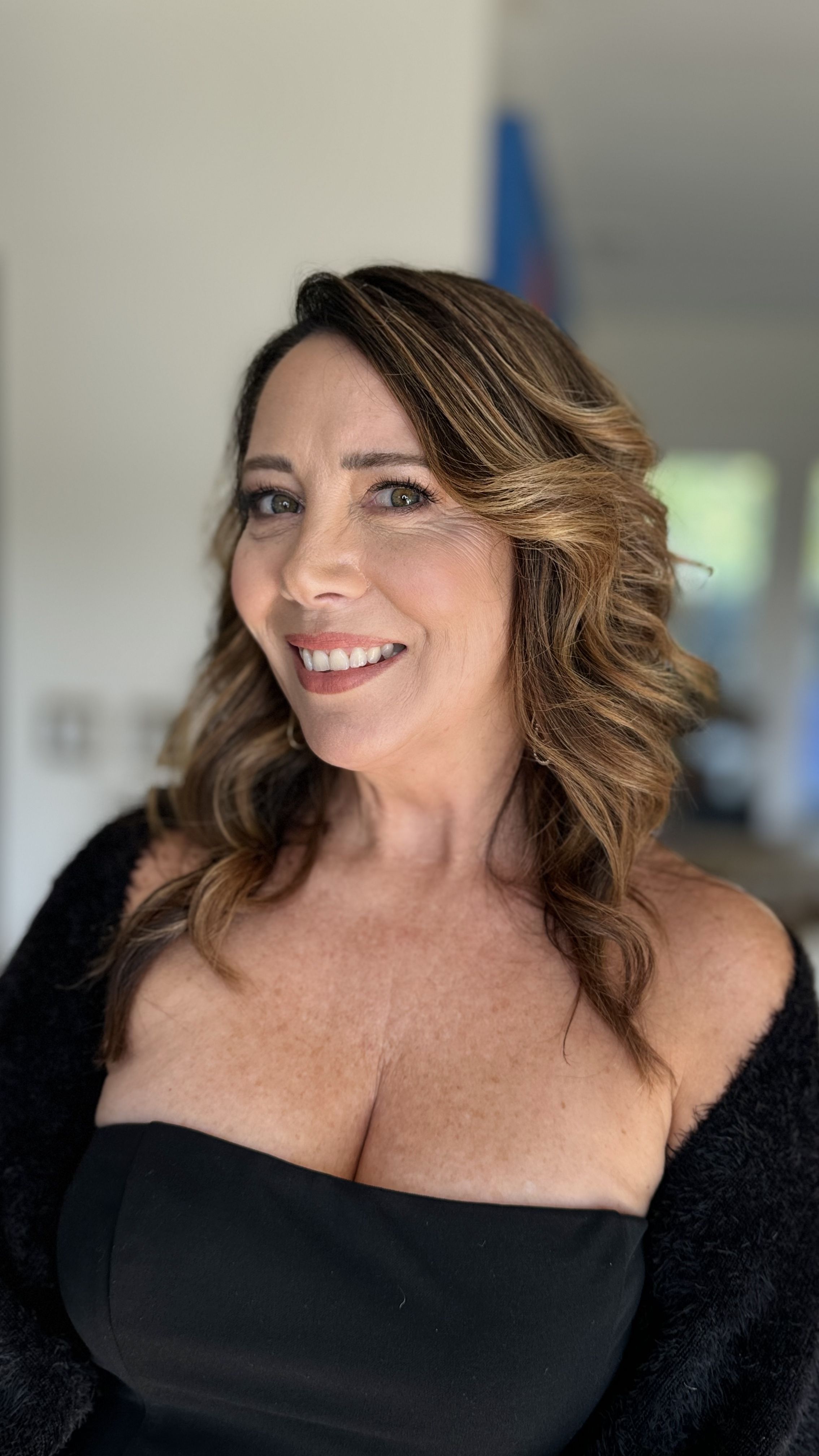 Smiling brunette woman with voluminous waves and soft neutral makeup.