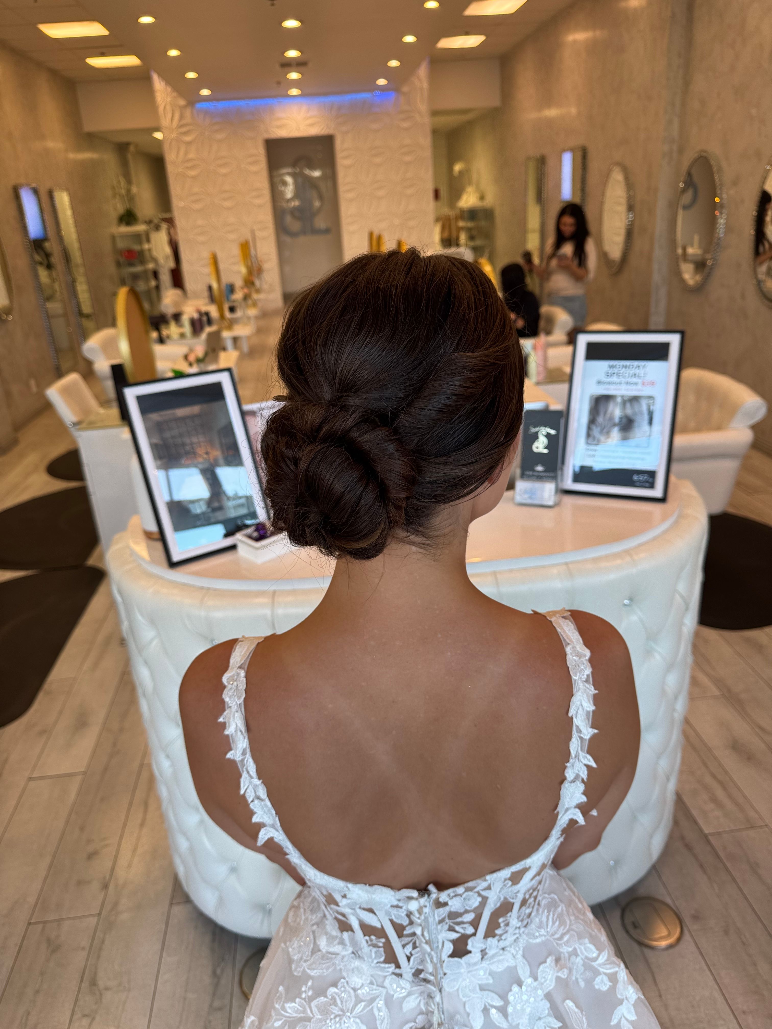 Back view of a textured low bridal updo with loose face-framing tendrils.