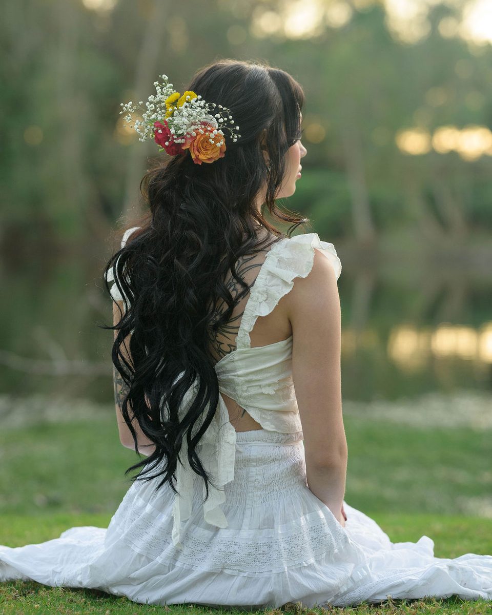 Back view of a bride with long dark curls in a half-up style accented with flowers.