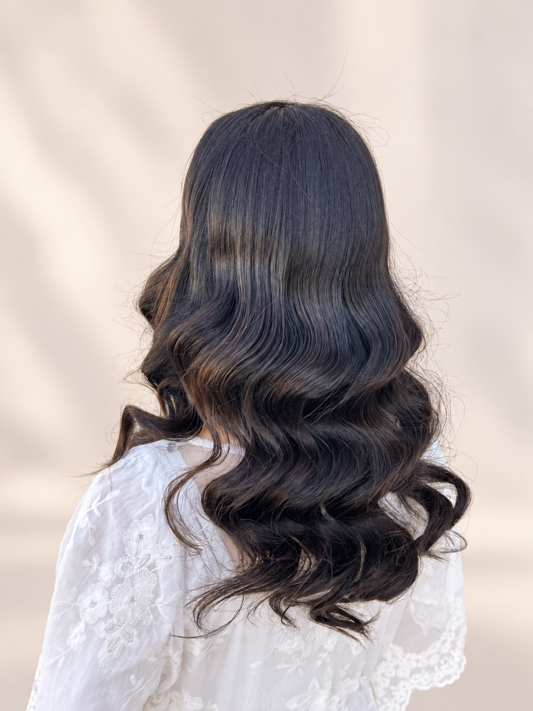 Back view of long dark hair styled in waves with a twisted half-up detail.