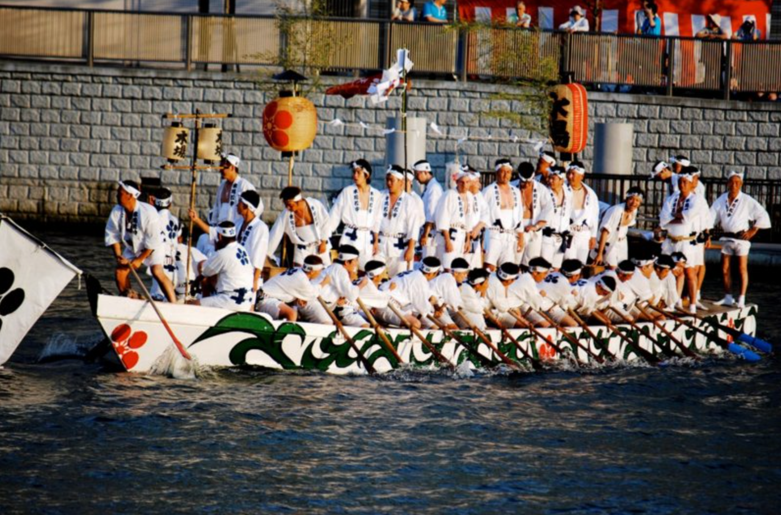 Men in white traditional attire rowing a large decorated boat during Tenjin matsuri festival