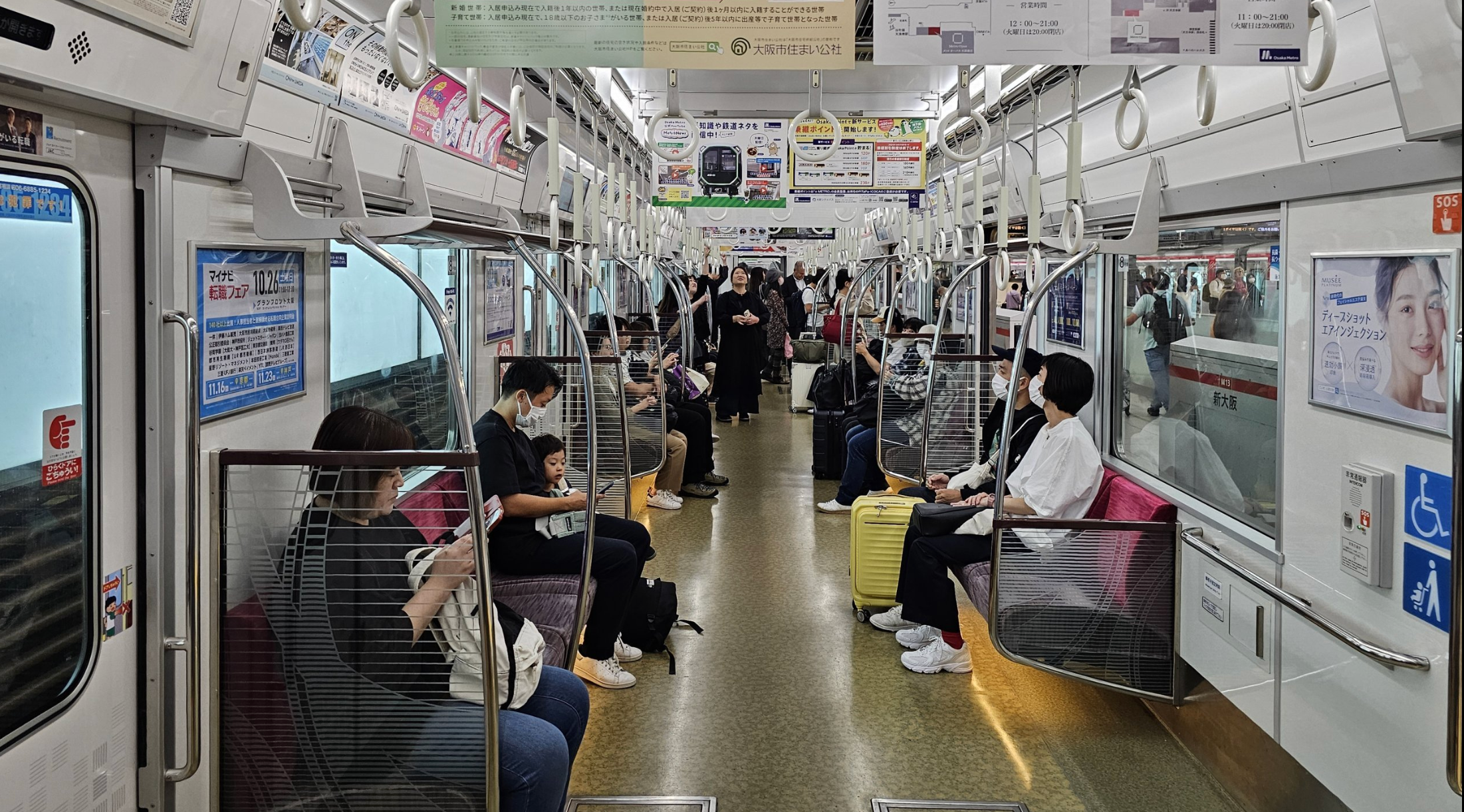 Interior of a Japanese subway train with seated passengers and various advertisements