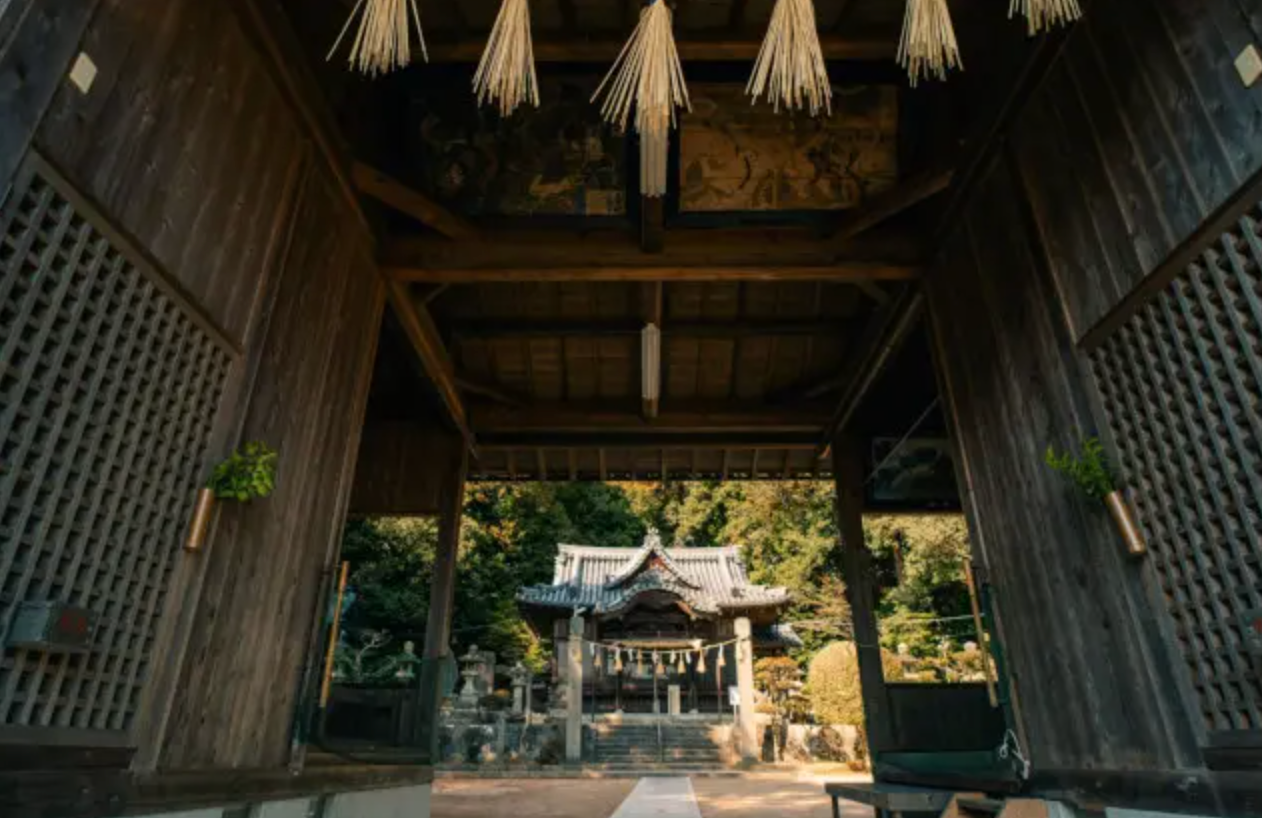View of a traditional Shinto shrine building through a wooden gateway with sacred ropes