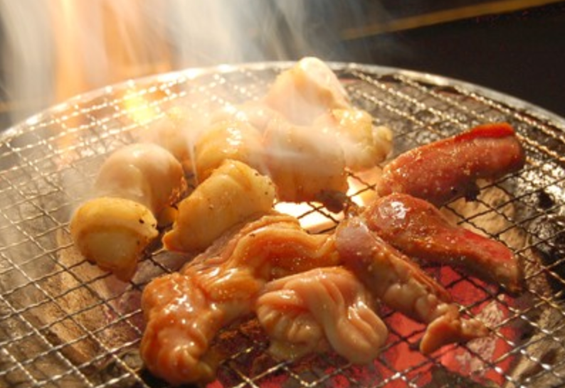 Assorted horumon offal grilling on a charcoal mesh with rising smoke