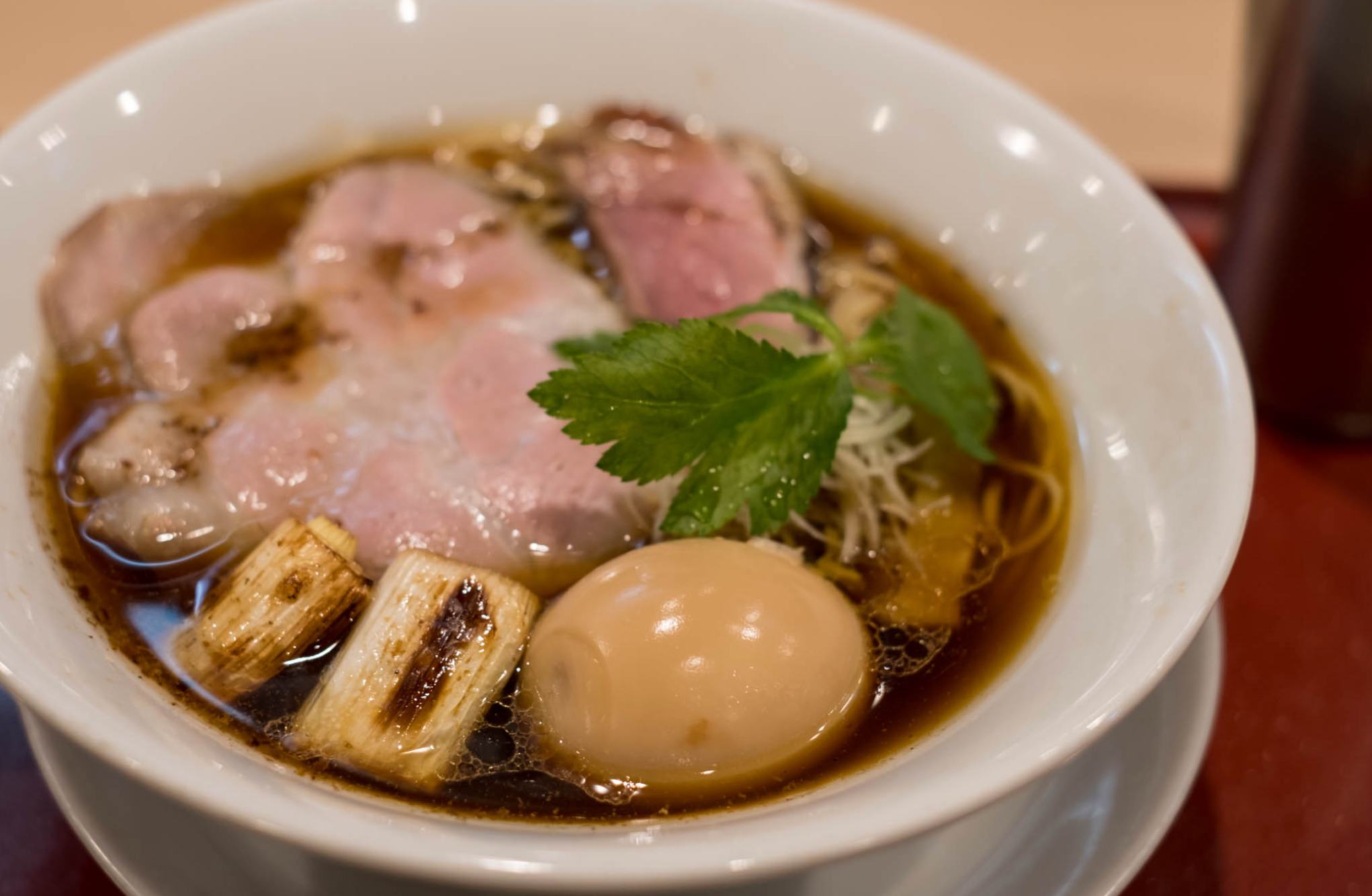 Shoyu ramen with chashu pork, a soft-boiled egg, and grilled leeks in a white bowl