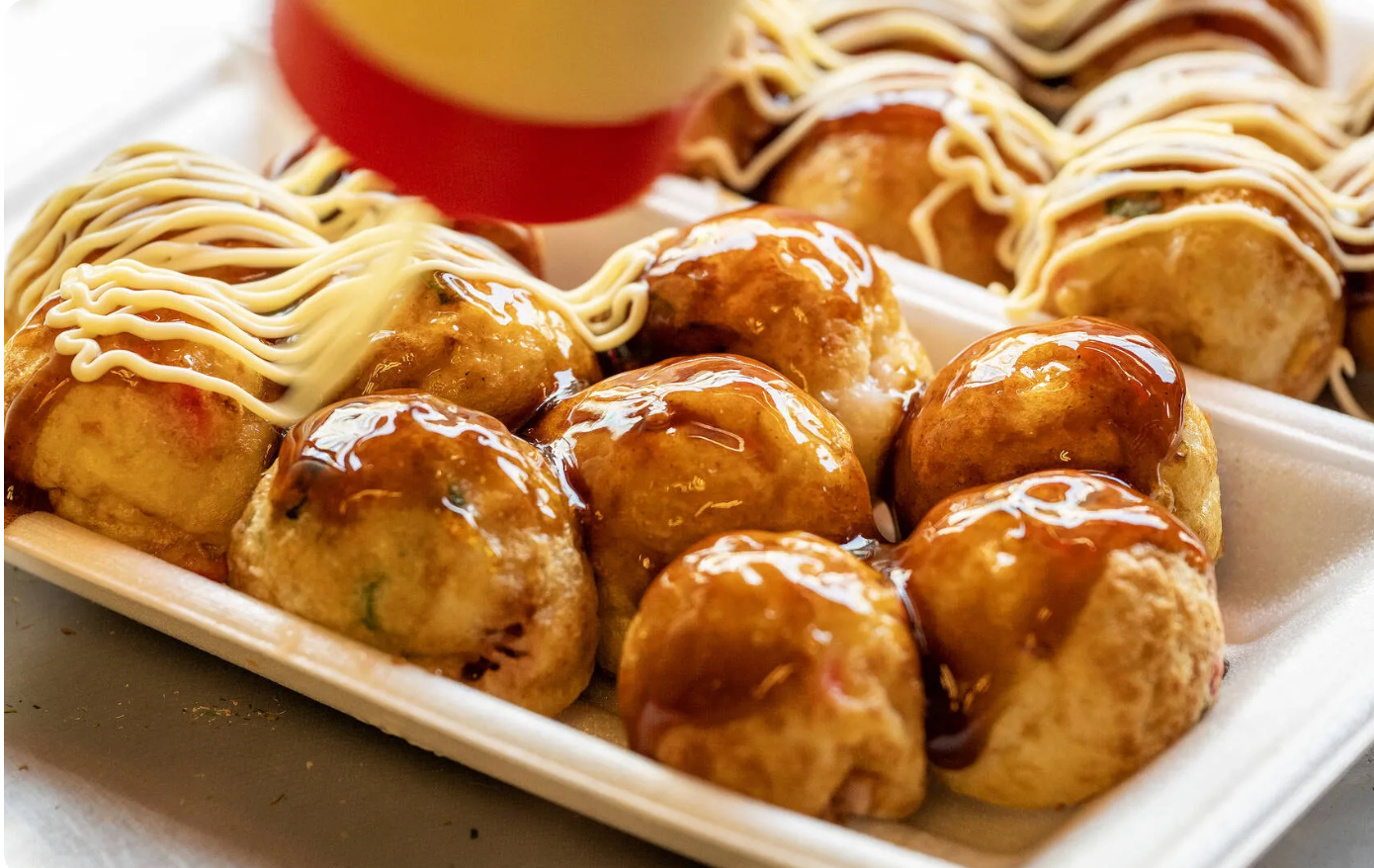 Japanese takoyaki octopus balls topped with sauce and being drizzled with mayonnaise