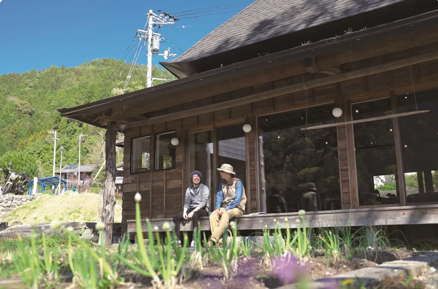 Two men sitting on the porch of a traditional wooden house in a rural setting
