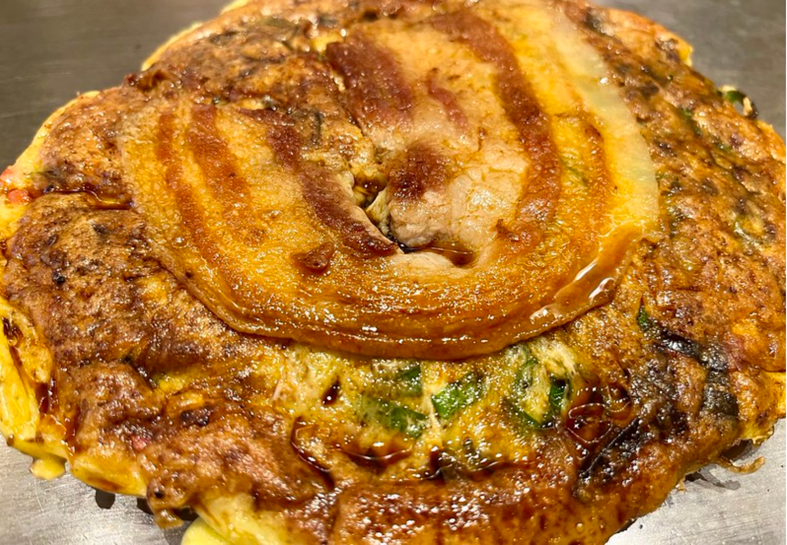 Savory Japanese negiyaki pancake topped with grilled pork belly