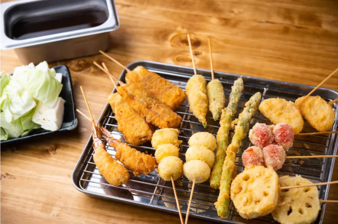 Assorted Japanese kushikatsu deep-fried skewers on a metal rack with cabbage and dipping sauce