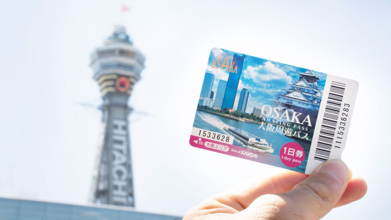 Hand holding an Osaka Amazing Pass in front of the Tsutenkaku Tower