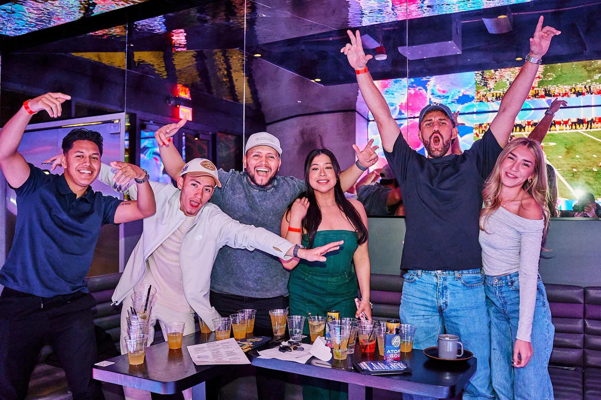 Group of friends celebrating at Atomic Golf with drinks and entertainment screens