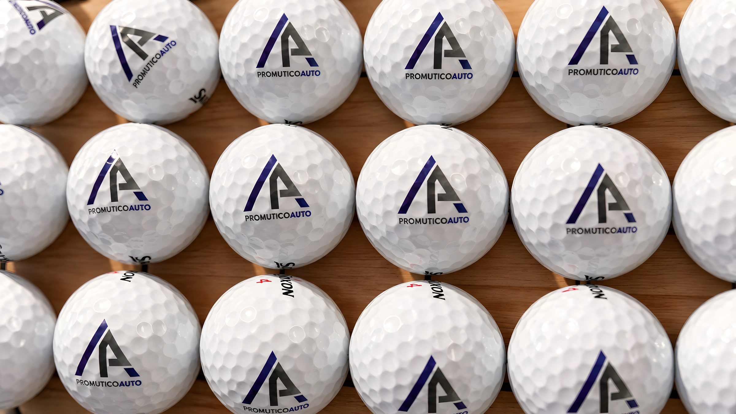 Palline da golf Srixon Z-Star con il logo Promutico Auto, allineate su un pannello di legno