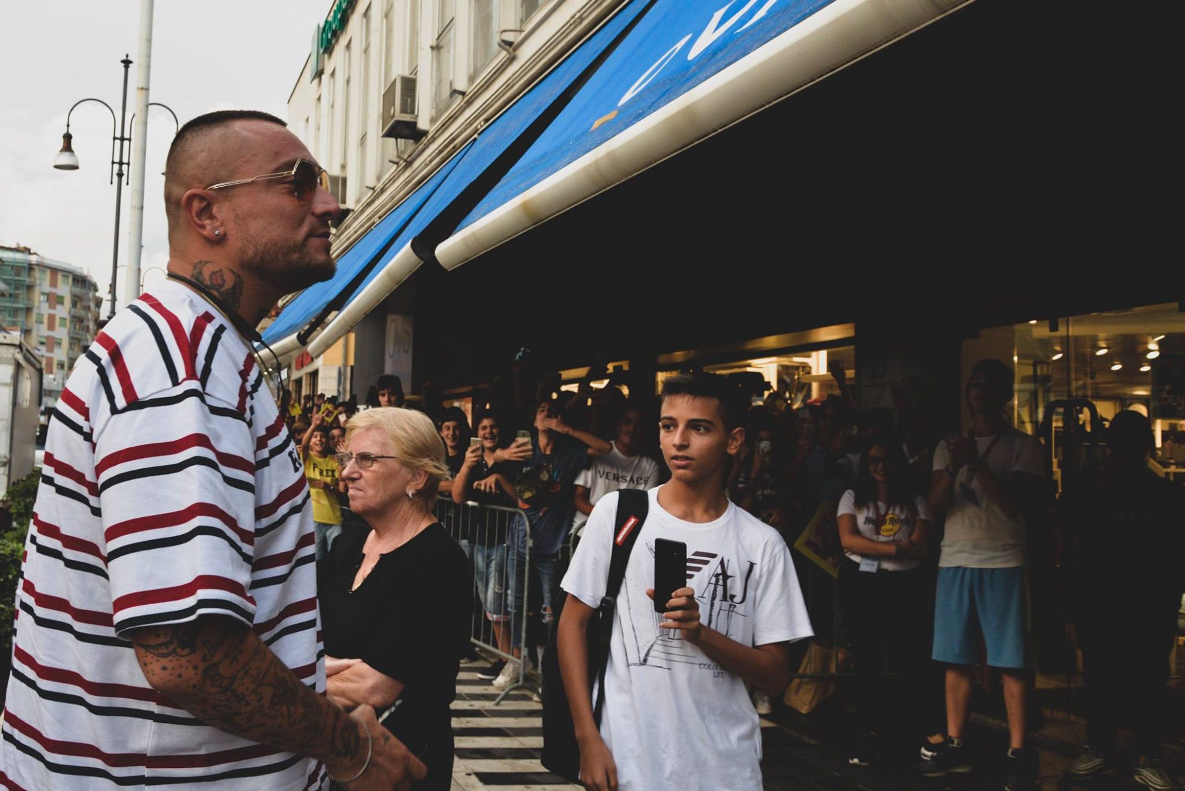 Un artista con una polo a righe all'ingresso del negozio, fra i fan in attesa