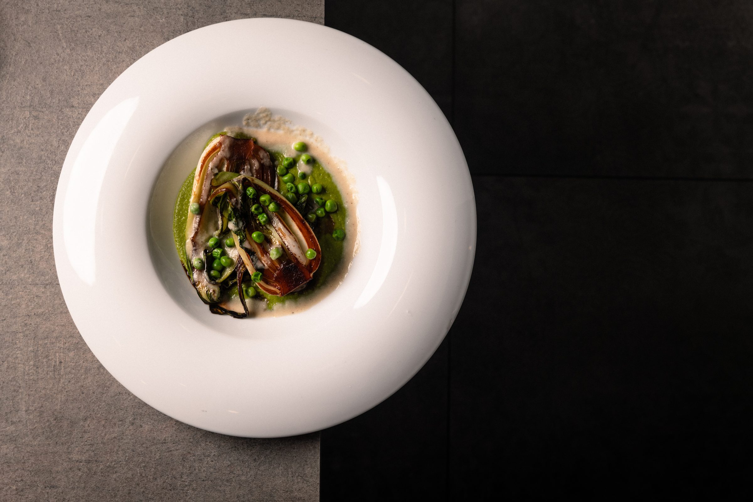 Un piatto fondo bianco con piselli e verdure grigliate, da ORA Ristorante