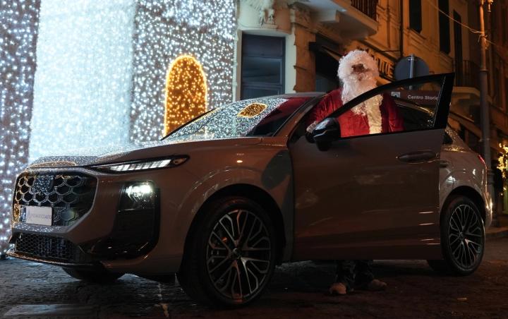 Babbo Natale apre la portiera di un SUV Audi fra le luminarie natalizie