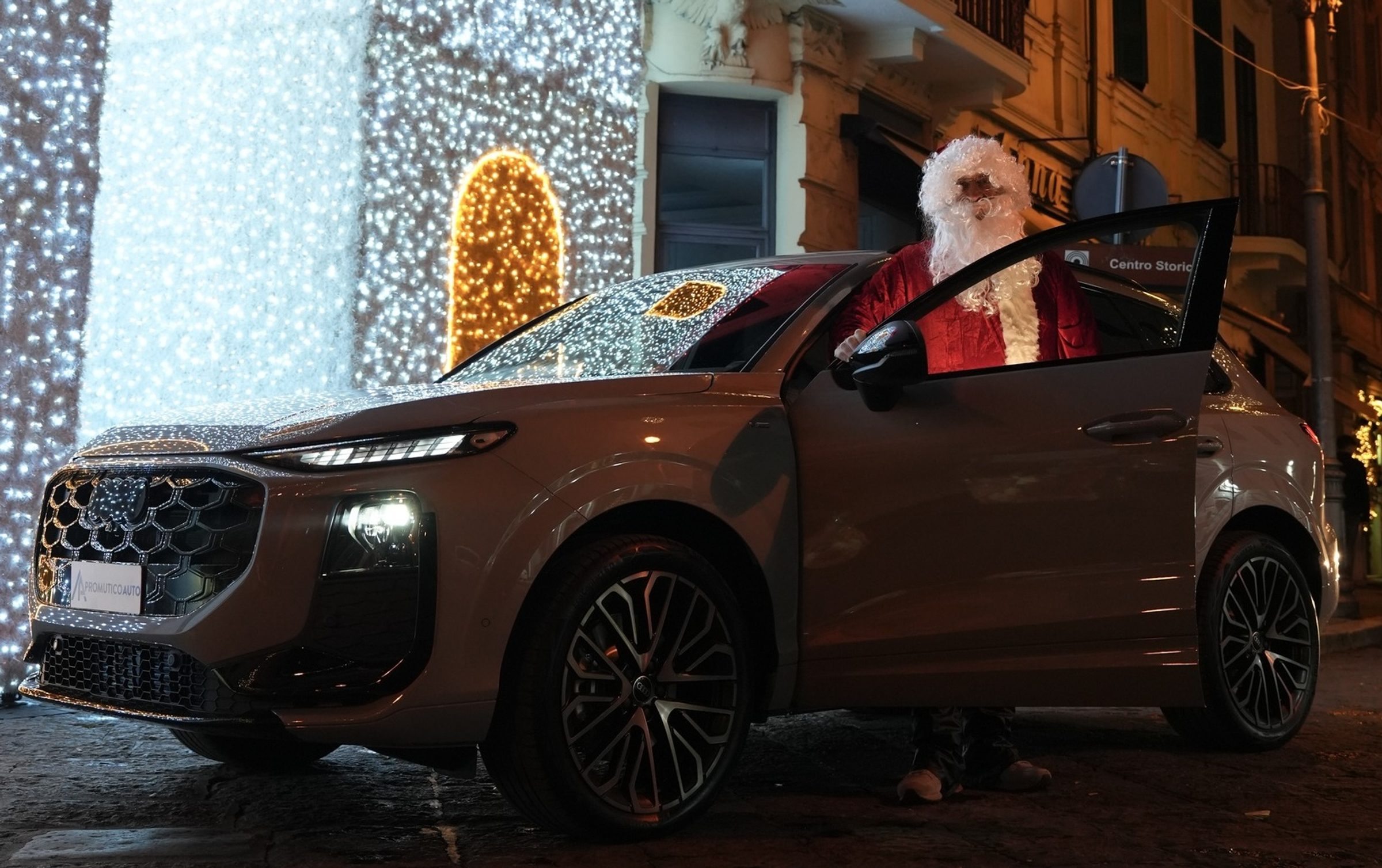 Babbo Natale apre la portiera di un SUV Audi fra le luminarie natalizie