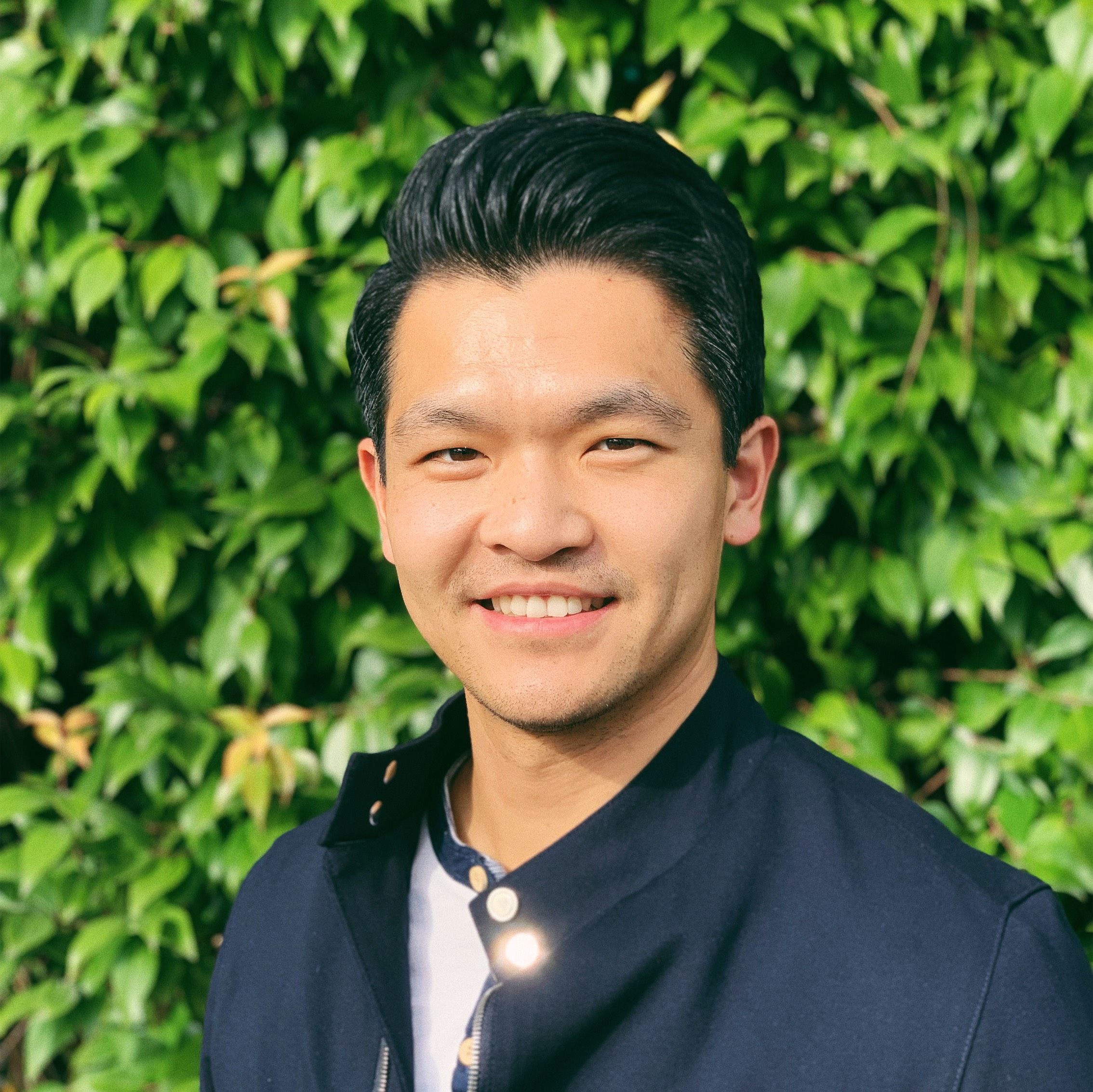 a man in a blue jacket is smiling in front of a tree .