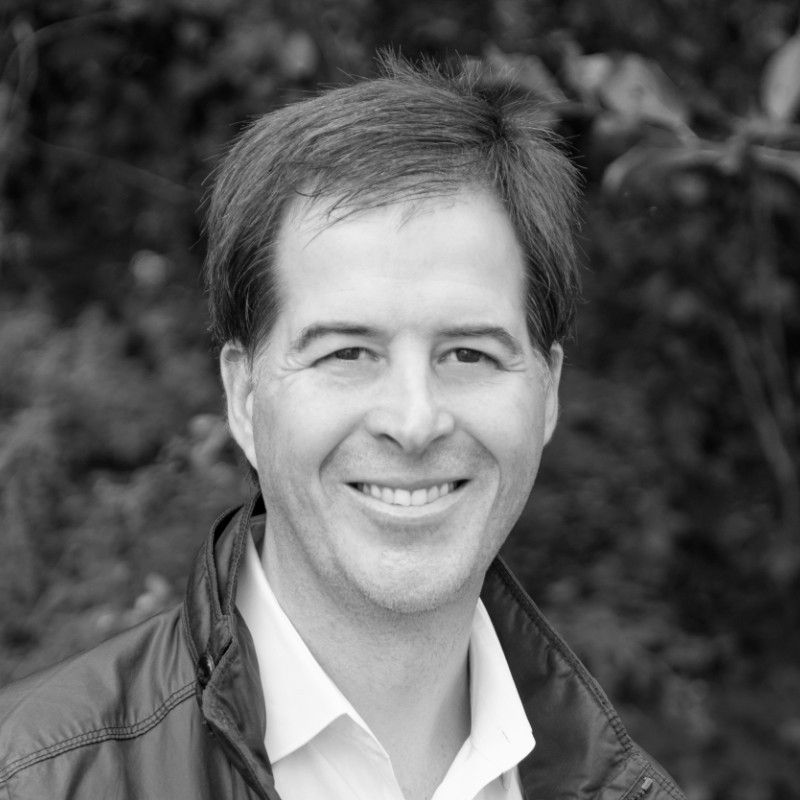 a man wearing a jacket and a white shirt smiles in a black and white photo