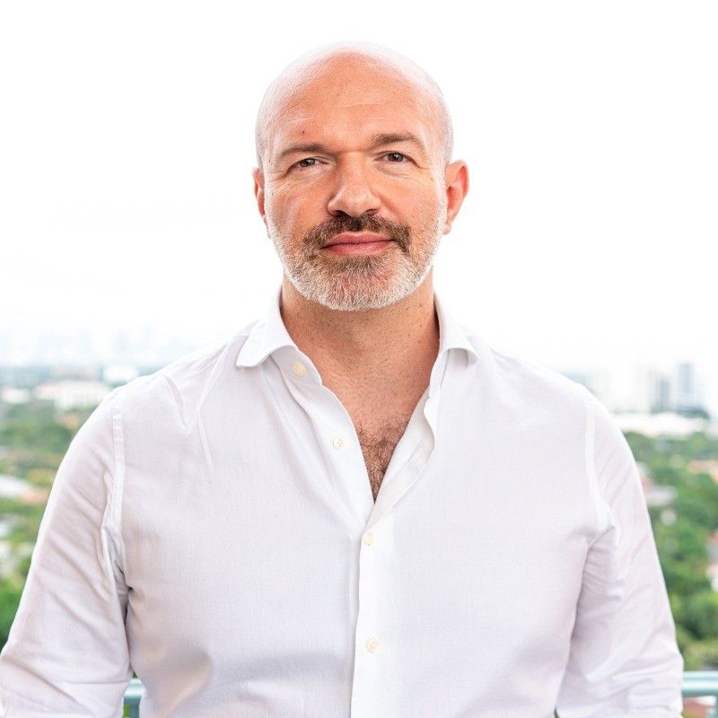 a bald man with a beard is wearing a white shirt and looking at the camera .