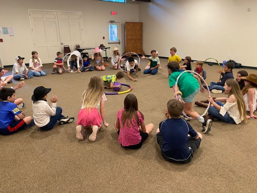 Campers sitting in a big circle enjoying a fun hula-hoop party game indoors.