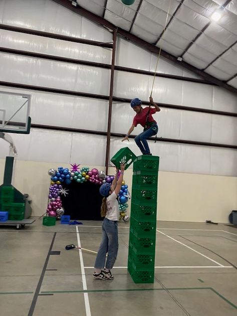 A brave camper balancing on a high tower of milk crates with a little help from a friend.