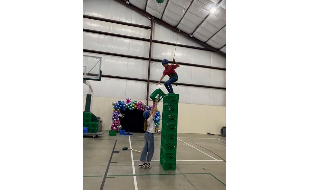 A brave camper balancing on a high tower of milk crates with a little help from a friend.