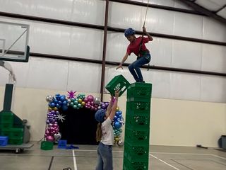 A brave camper balancing on a high tower of milk crates with a little help from a friend.