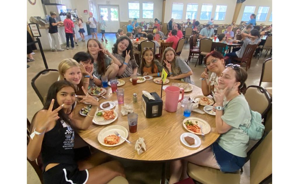 A happy table of campers flashing peace signs and enjoying lunch together.