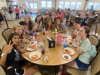 A happy table of campers flashing peace signs and enjoying lunch together.