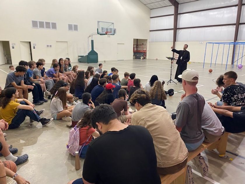 Father speaking to a big group of attentive campers gathered in the gym.