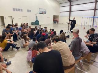 Father speaking to a big group of attentive campers gathered in the gym.