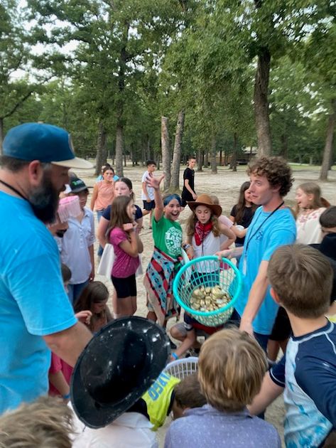 A counselor holding up a basket of prizes while campers cheer and reach out around him.