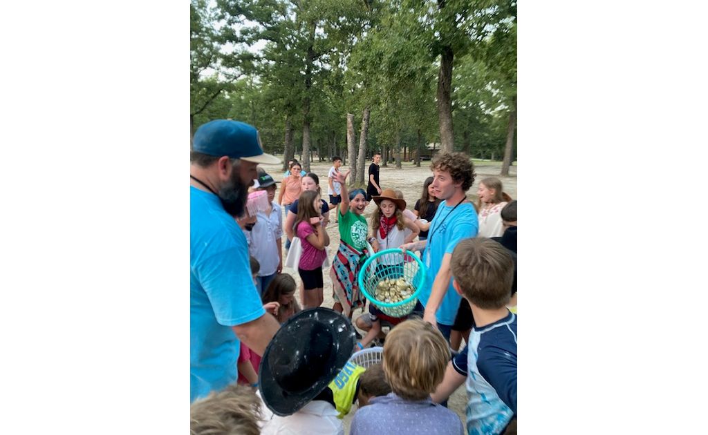 A counselor holding up a basket of prizes while campers cheer and reach out around him.