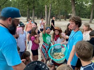 A counselor holding up a basket of prizes while campers cheer and reach out around him.