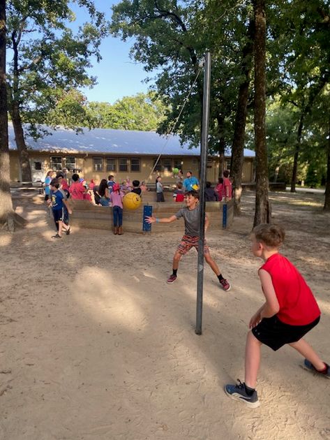 Campers having a blast playing tetherball under the shade of the trees.