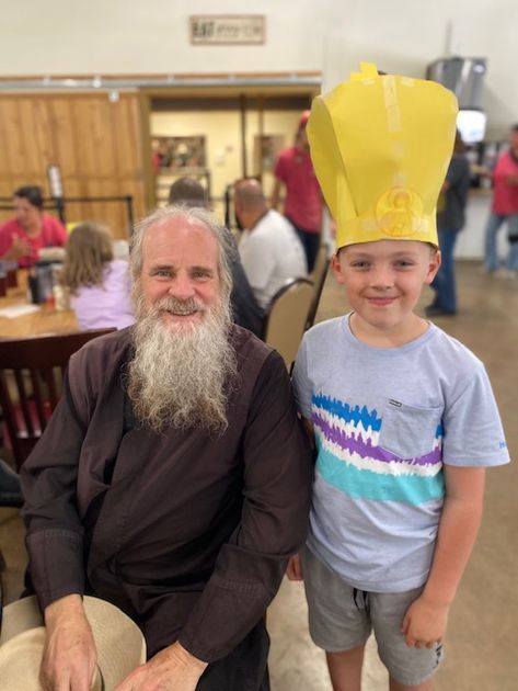 A young camper wearing a homemade paper bishop's crown posing proudly with His Grace Bishop Gerasim