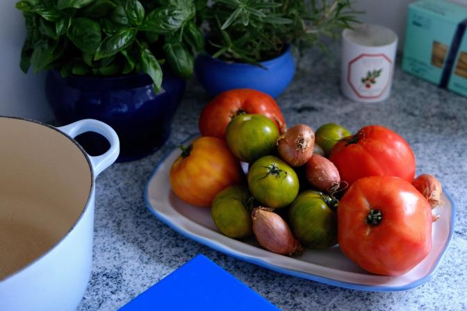Fat med tomater i olika färger och storlekar. Bredvid står en gryta och bakom står två basilikaplantor. 