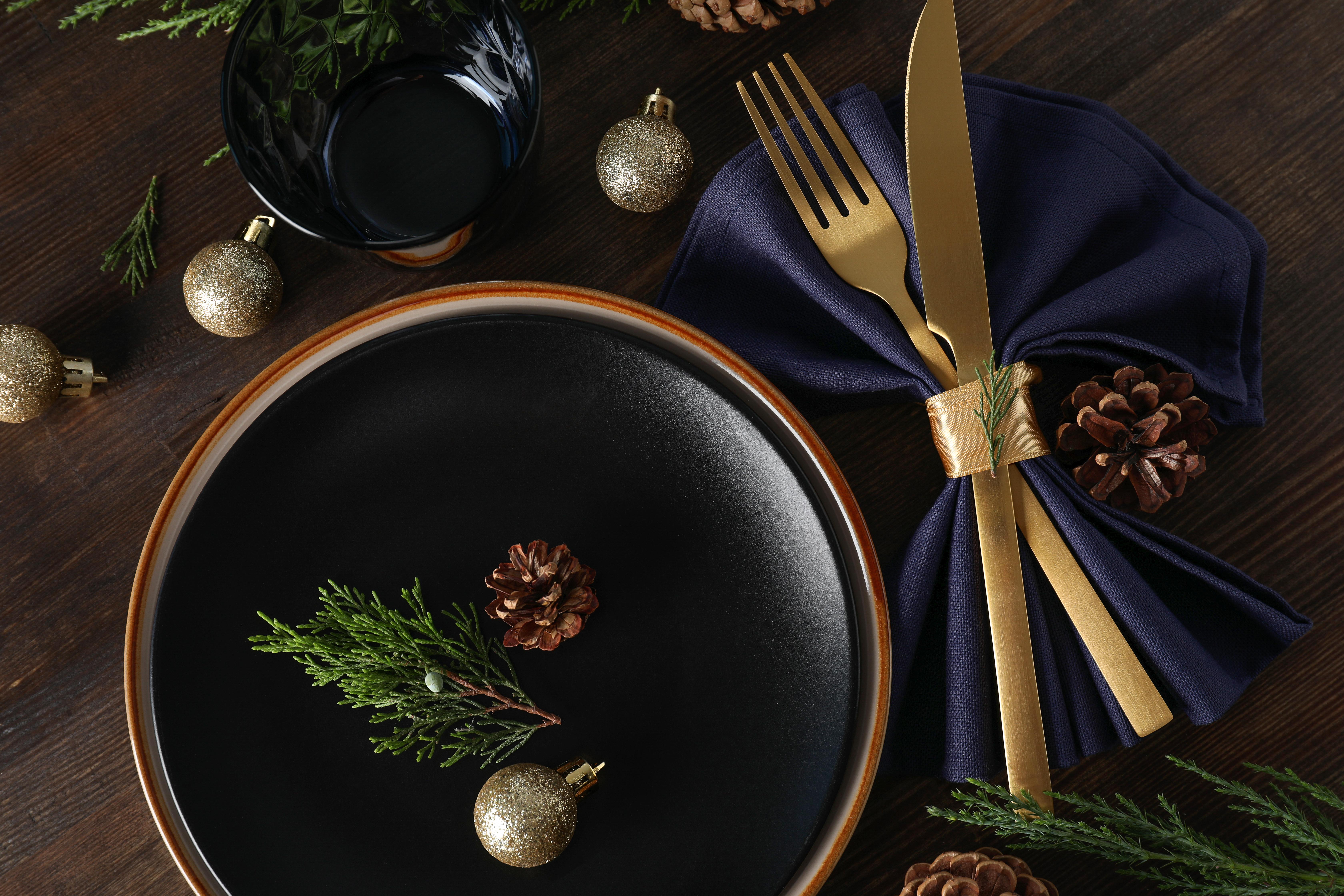 Bord som dukats inför festmåltid med gyllene bestick och julgranskulor på bordet.