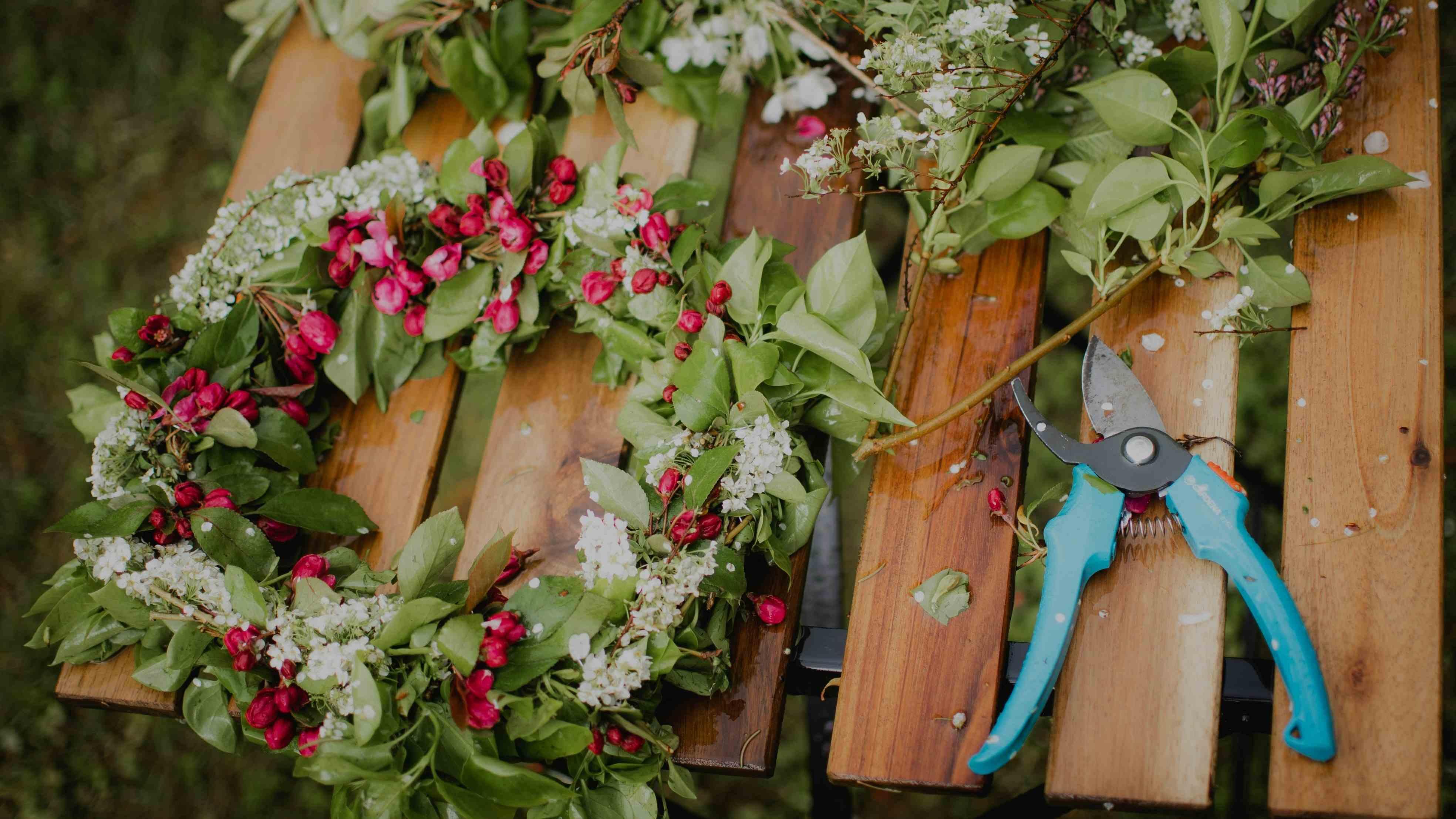 Midsommarkrans på en bänk. Bredvid ligger blommor som blivit över och en sax.