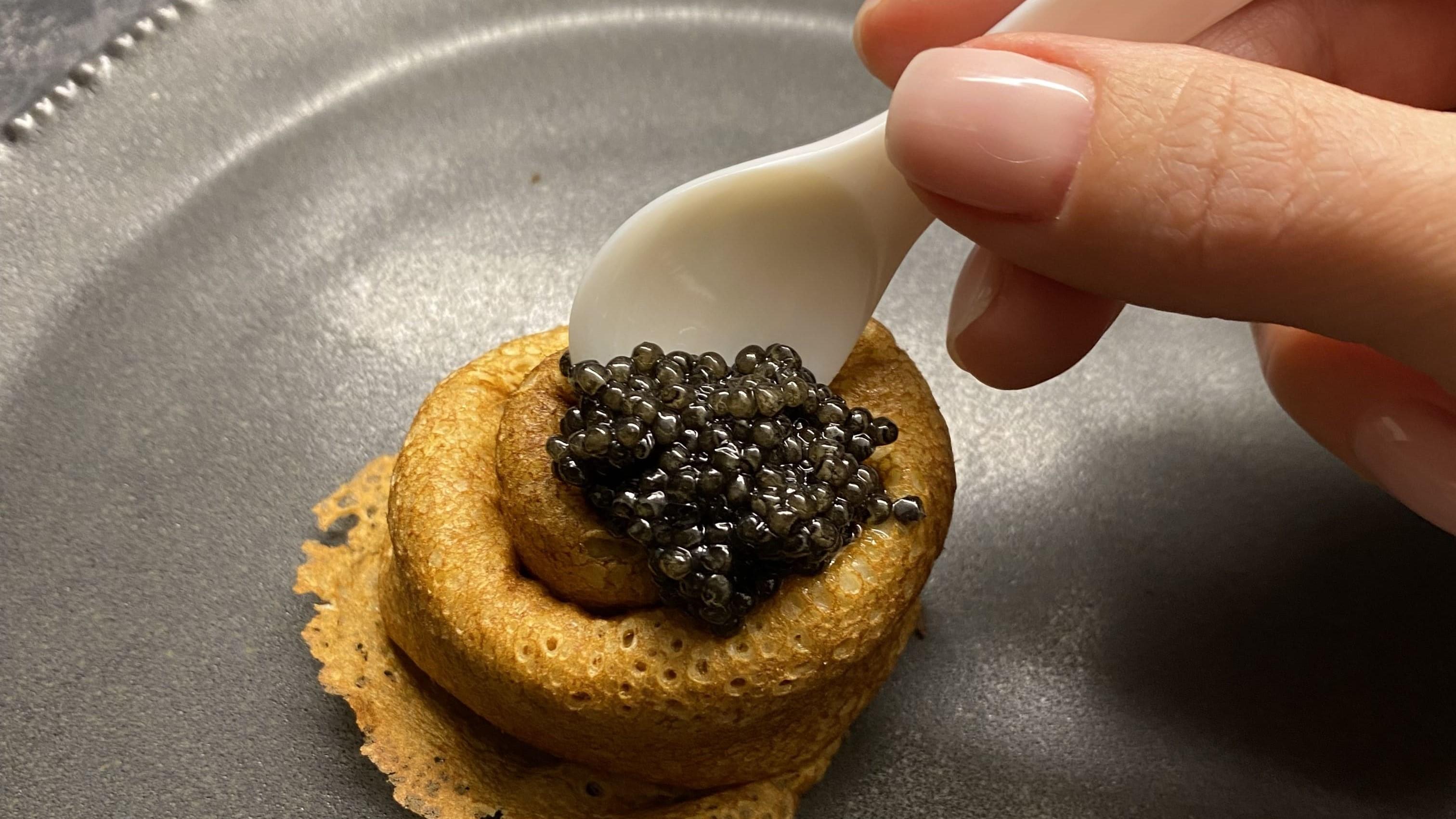 Hoprullad pannkaka toppad med kaviar som någon lägger dit med en pärlemorsked.