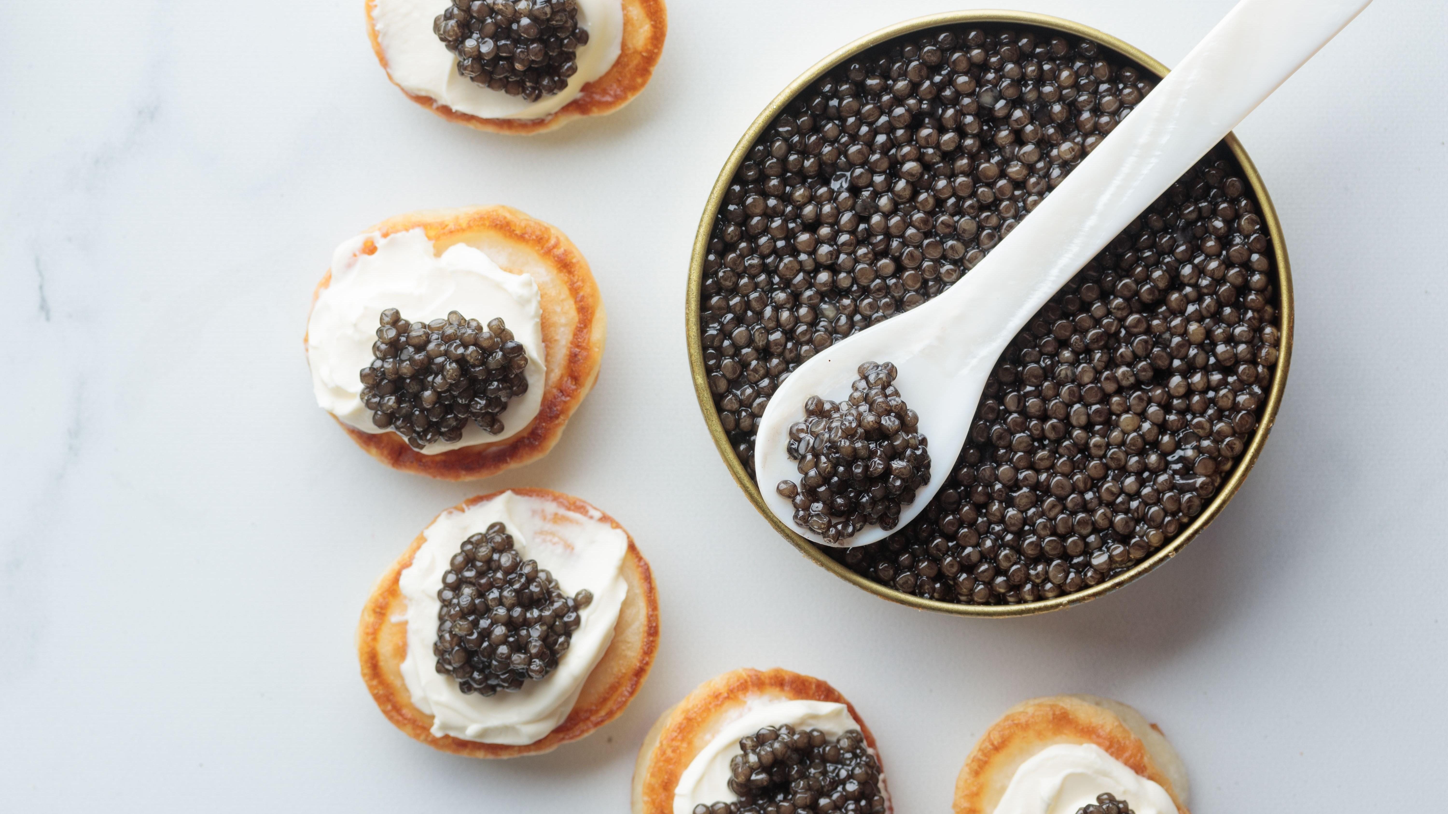 Kaviarburk med pärlemorsked, omringad av blinier med smetana och kaviar.
