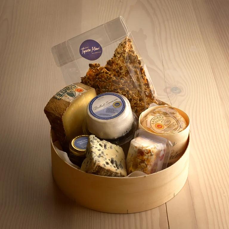 Rund trälåda full med olika sorters ost. Lådan står på ett träbord. 