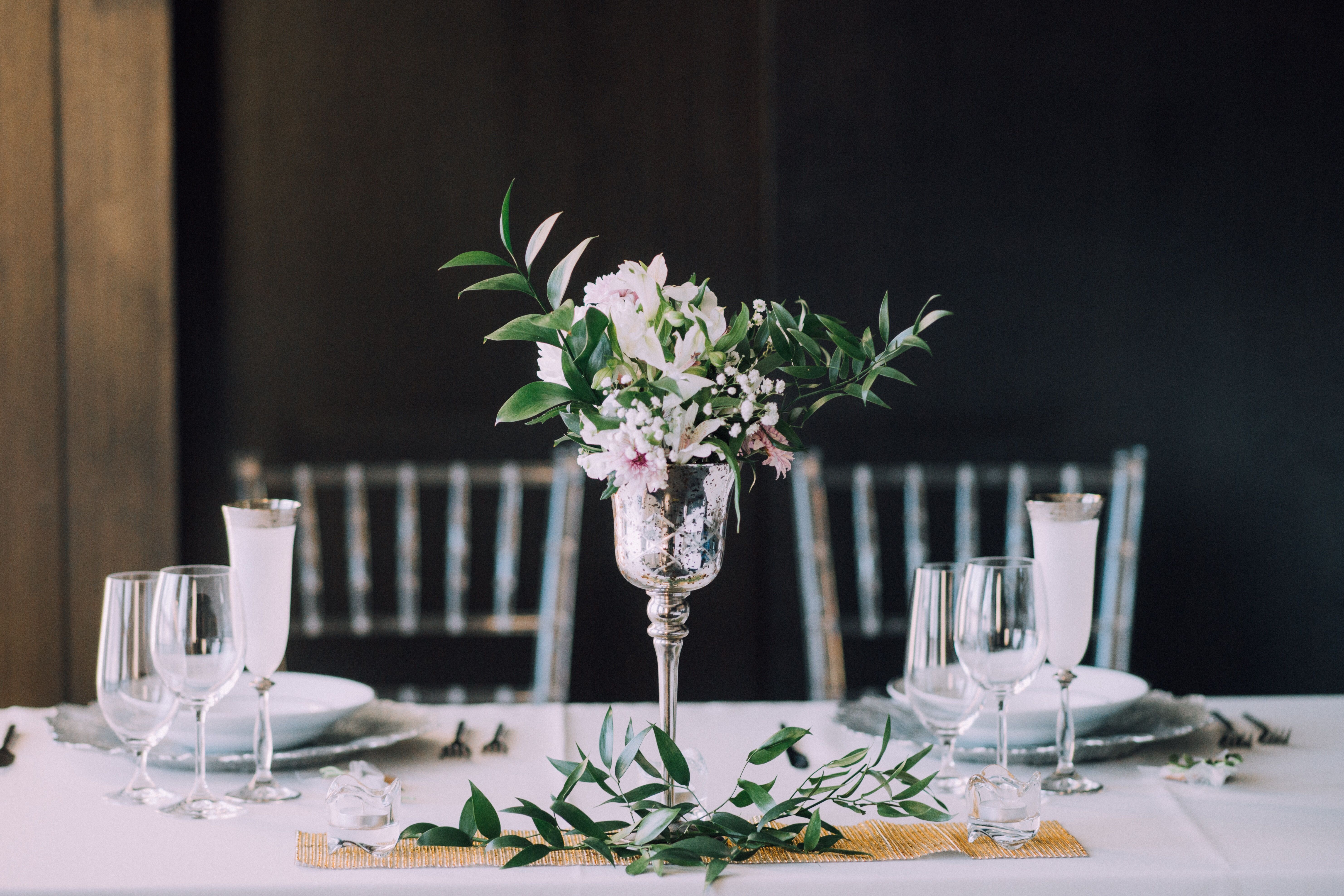 Vackert dukat bord med ett glas med blommor och växter i mitten. 